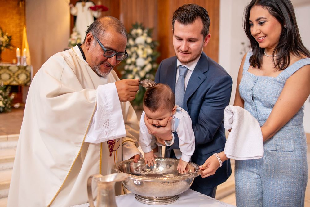 Priest blessing baby during baptism ceremony with parents inside church in Guatemala City