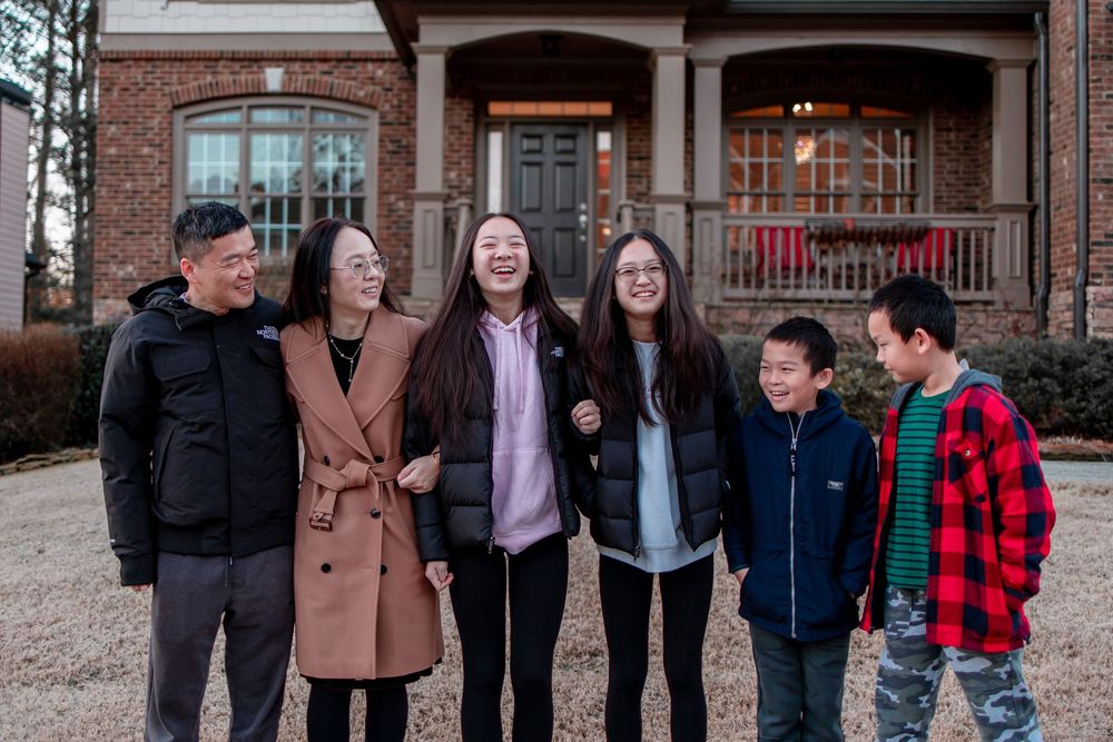 Family standing together outdoors in front of house during casual photo session