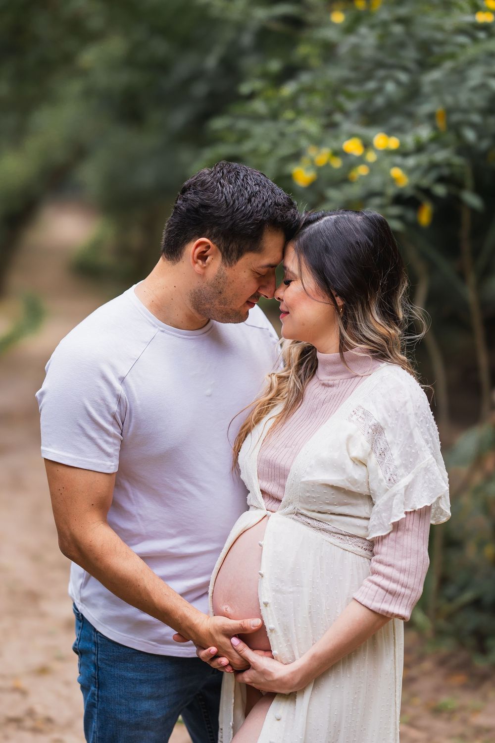 Expecting couple standing close together, hands on baby bump during outdoor maternity session.