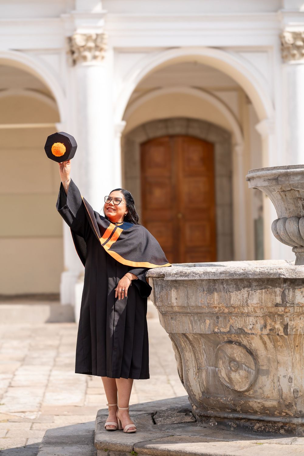 Graduate in cap and gown posing in colonial hallway at San Carlos University, Guatemala City