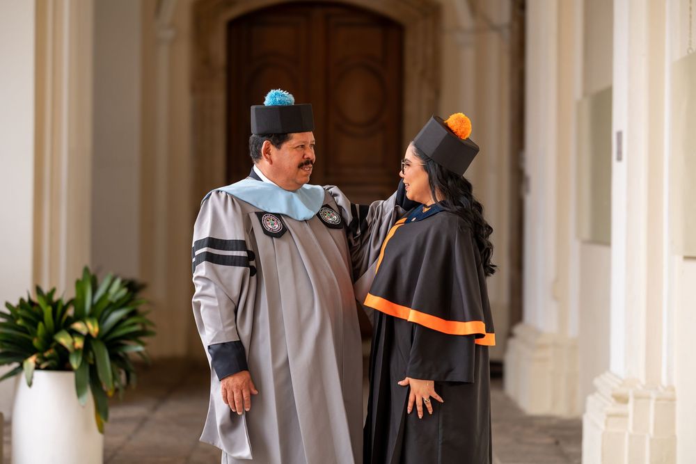 Graduate in cap and gown posing with dad in colonial hallway at San Carlos University, Guatemala City