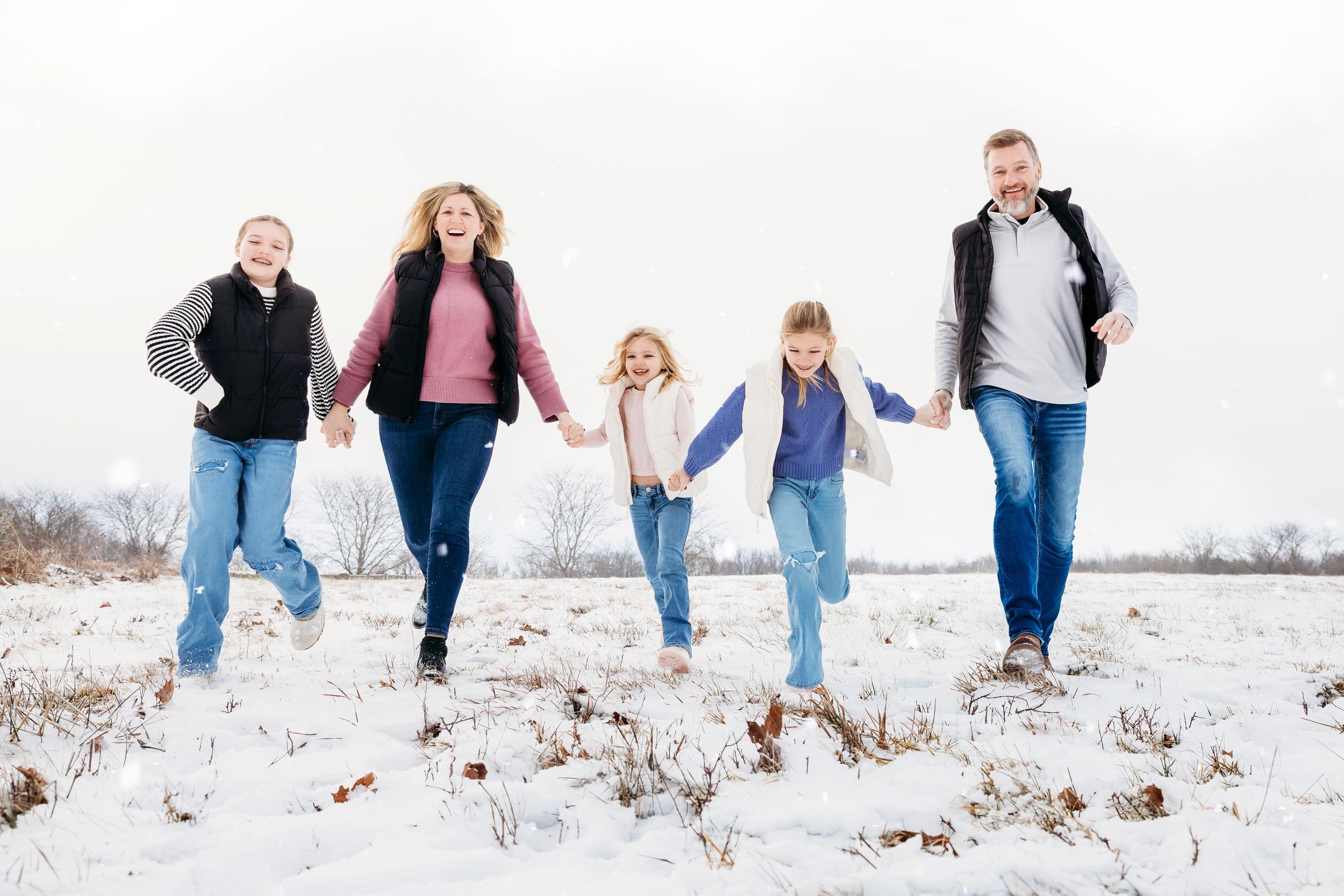 A group of people joyfully running together through a snowy field on a winter day.
