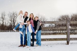 A group poses together in winter attire against a snowy landscape with wooden fencing in the background.
