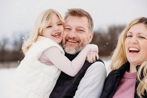 Happy family laughing together outdoors in winter with snow falling around them.