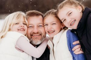 A joyful winter portrait of a family hugging and smiling together in the snow.