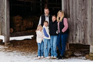 A group stands together against a rustic wooden barn in winter with snow on the ground.