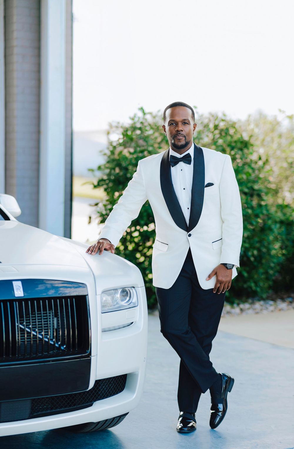 Luxury white Rolls Royce car parked at an elegant venue with formal attire and pillars in the background.