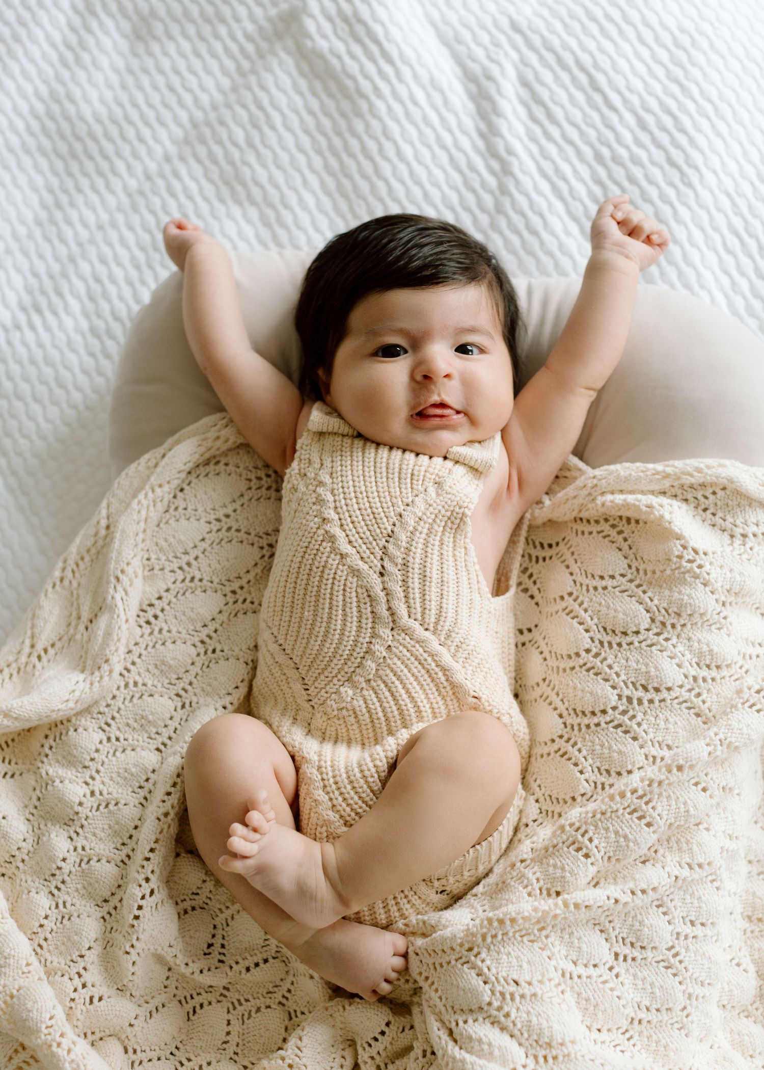 Baby wrapped in cozy white knit blanket with pacifier looking up at camera.