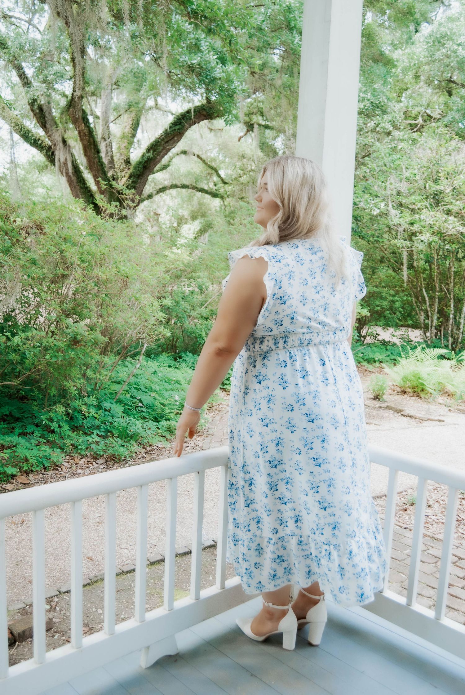 White porch railing and steps with someone wearing a blue floral dress in a garden setting.