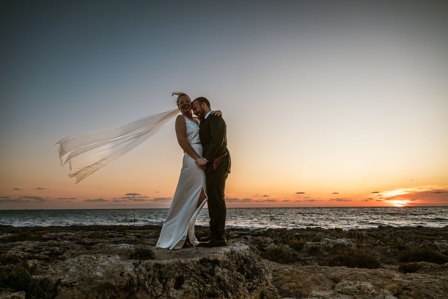 Trouwkoppel bij zonsondergang aan zee tijdens destination wedding, vastgelegd door Bart Boodts met focus op romantiek en vrijheid.