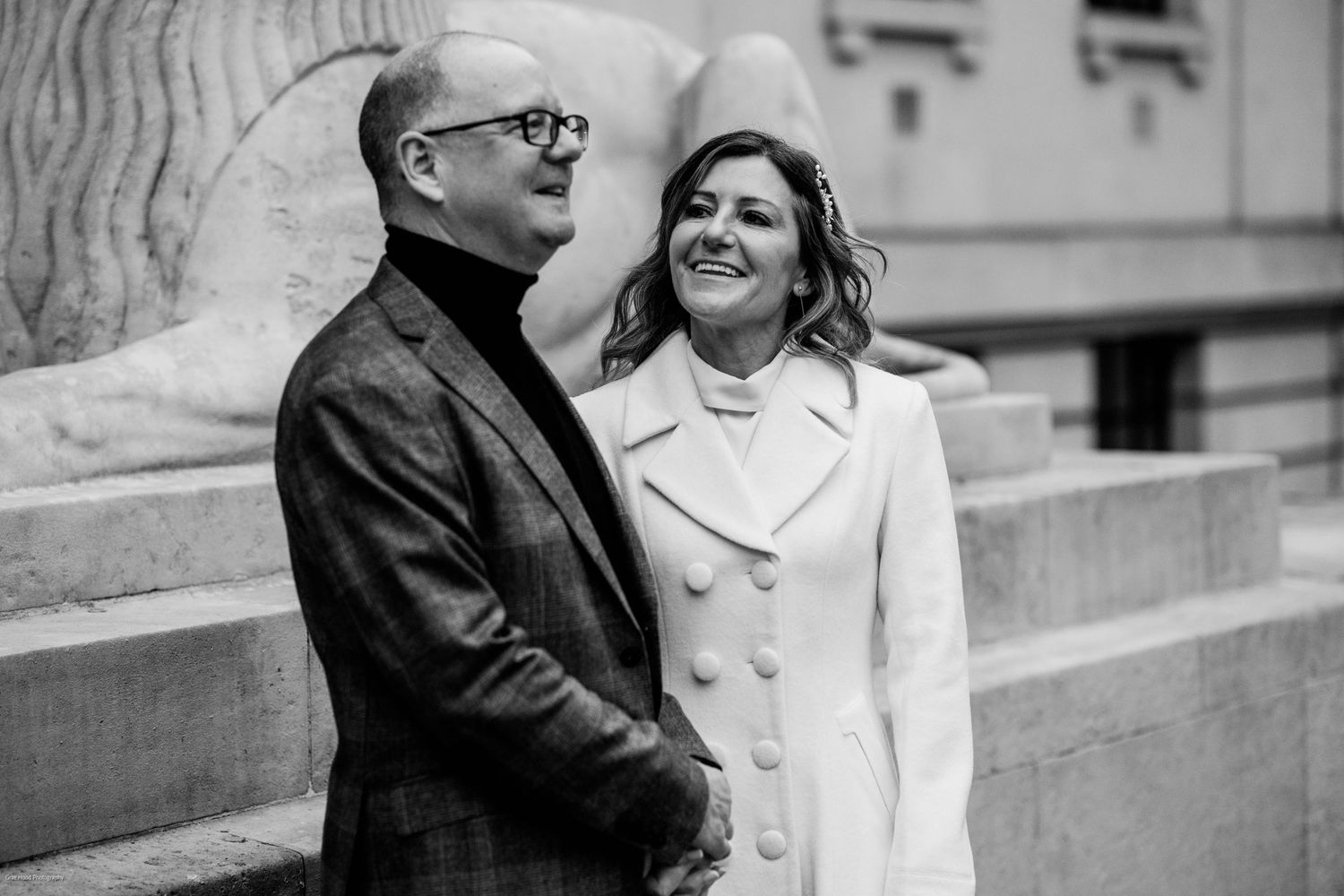 A couple in formal attire laughs together while sitting on outdoor stone steps.