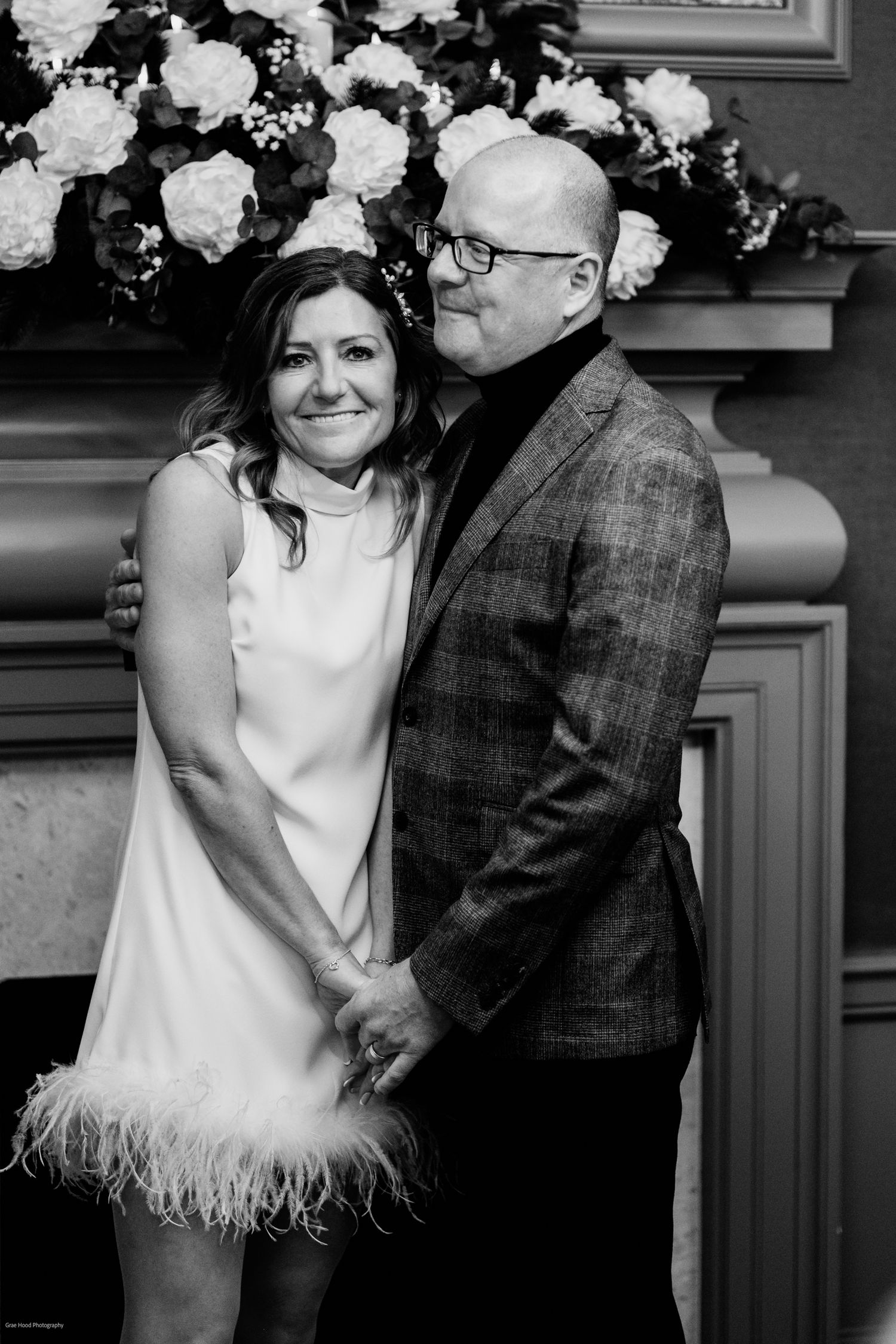 A couple in formal attire share an intimate moment during their wedding celebration in black and white photography.