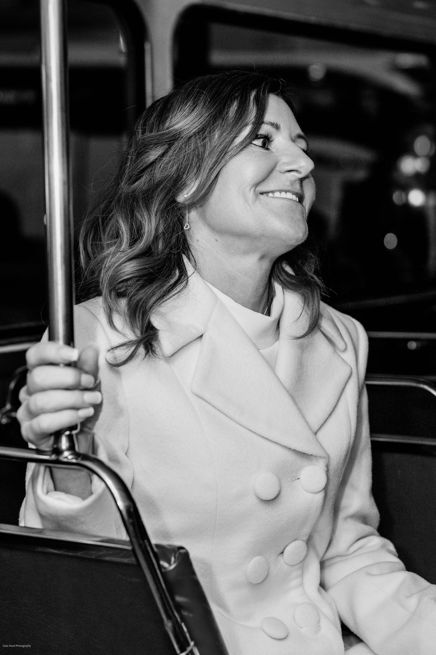 Black and white photo series showing a person in a white coat with large buttons smiling and posing on a pole.