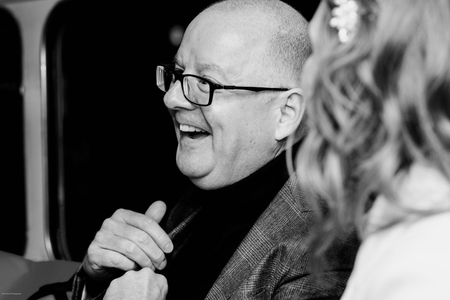 Black and white photo showing two people in conversation wearing glasses and smiling warmly.
