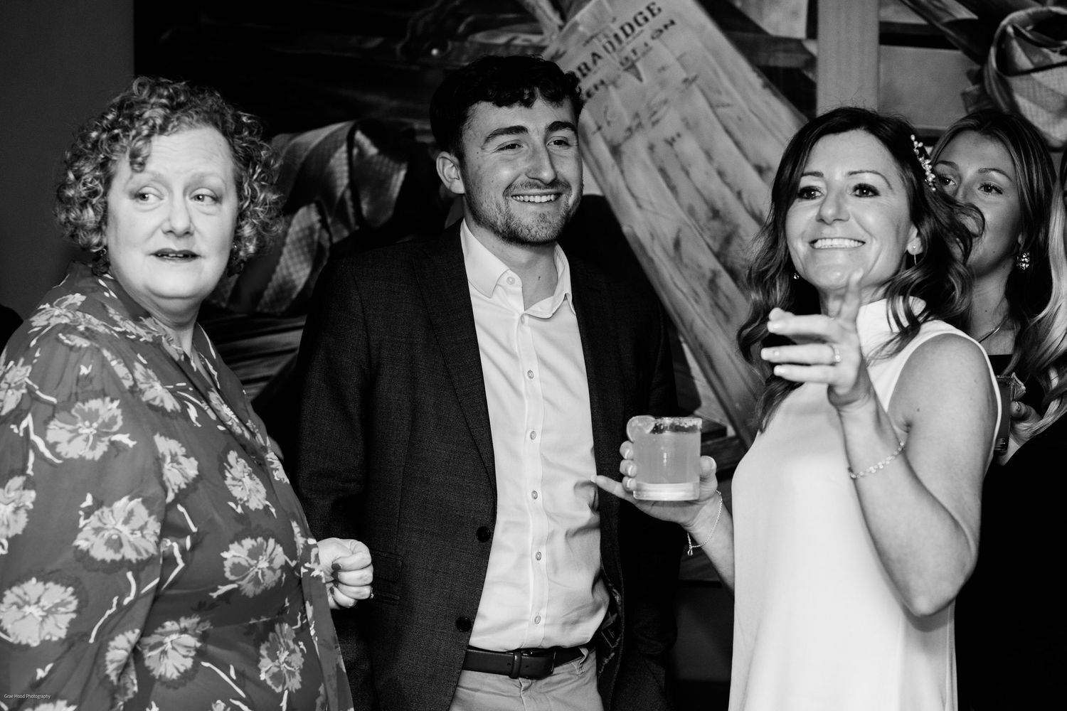 A black and white photo shows guests enjoying drinks and laughing together at a social gathering.