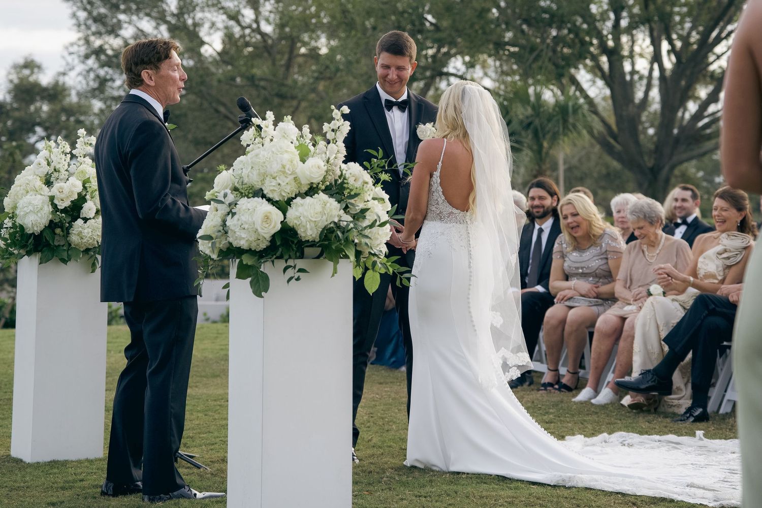 Outdoor wedding ceremony with white chairs and floral arrangements set up on a lush green lawn.