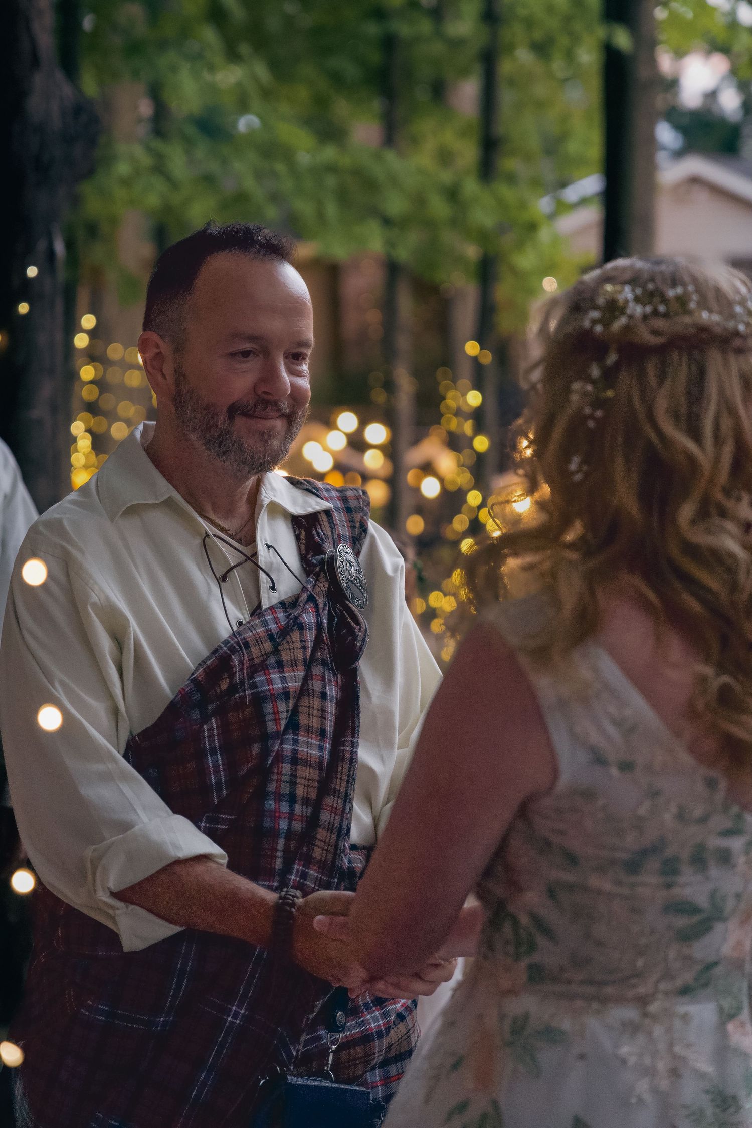 A couple shares a joyful dance together at an outdoor evening reception with string lights twinkling in the background.