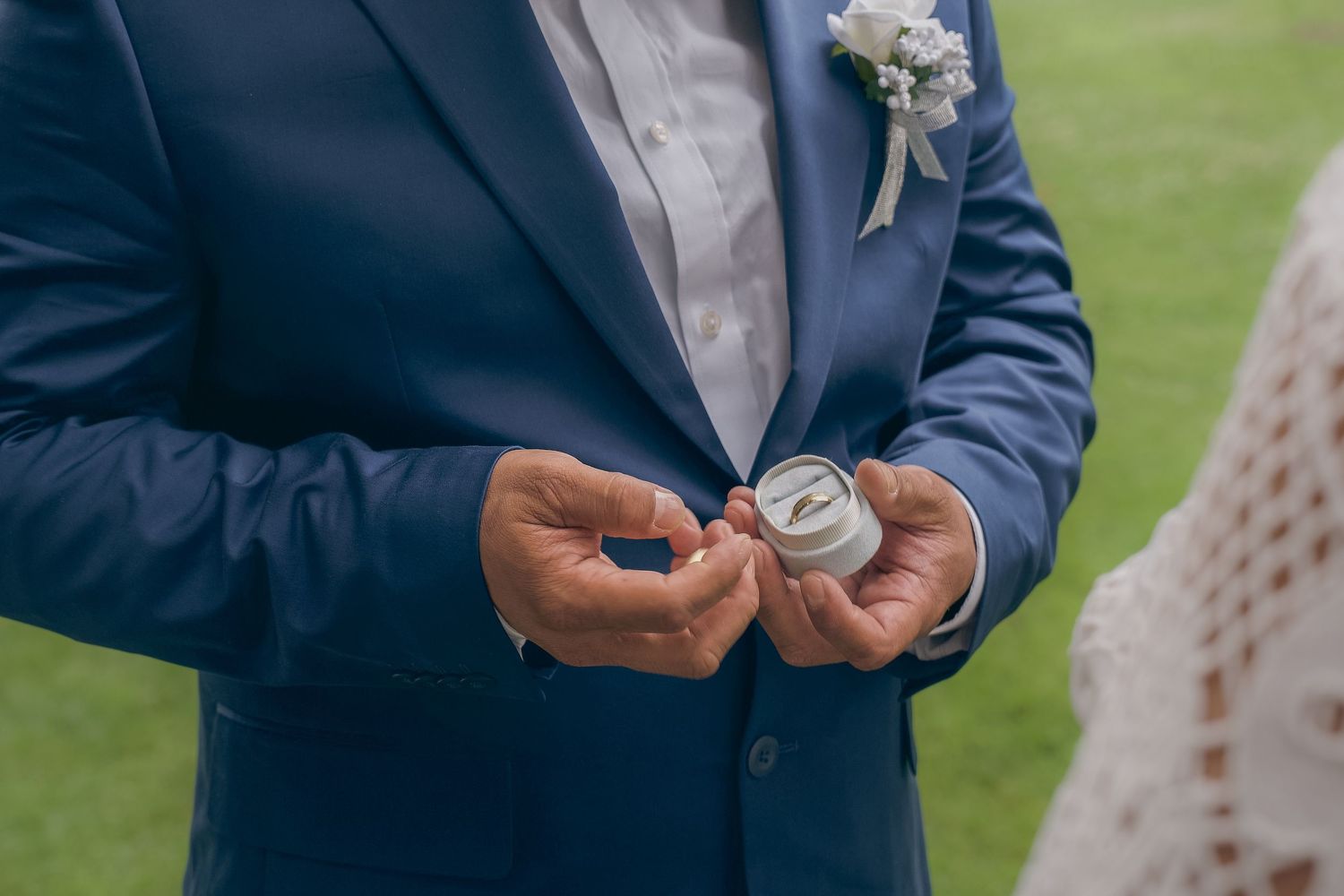 A person in a blue suit jacket holds and examines a small blue object outdoors on a sunny day.