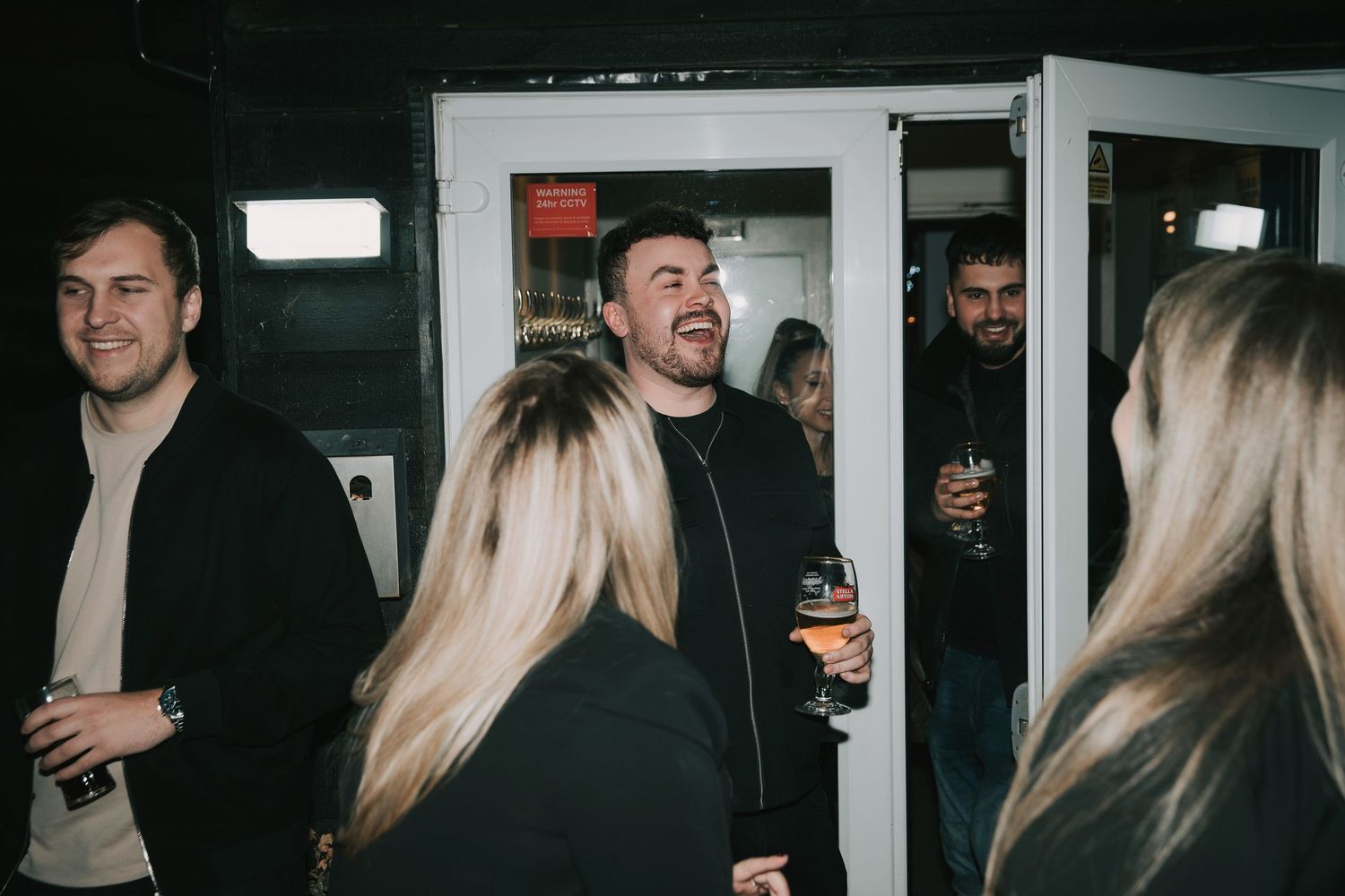 A group of people gathered in a dimly lit space with white door frames visible in the background.