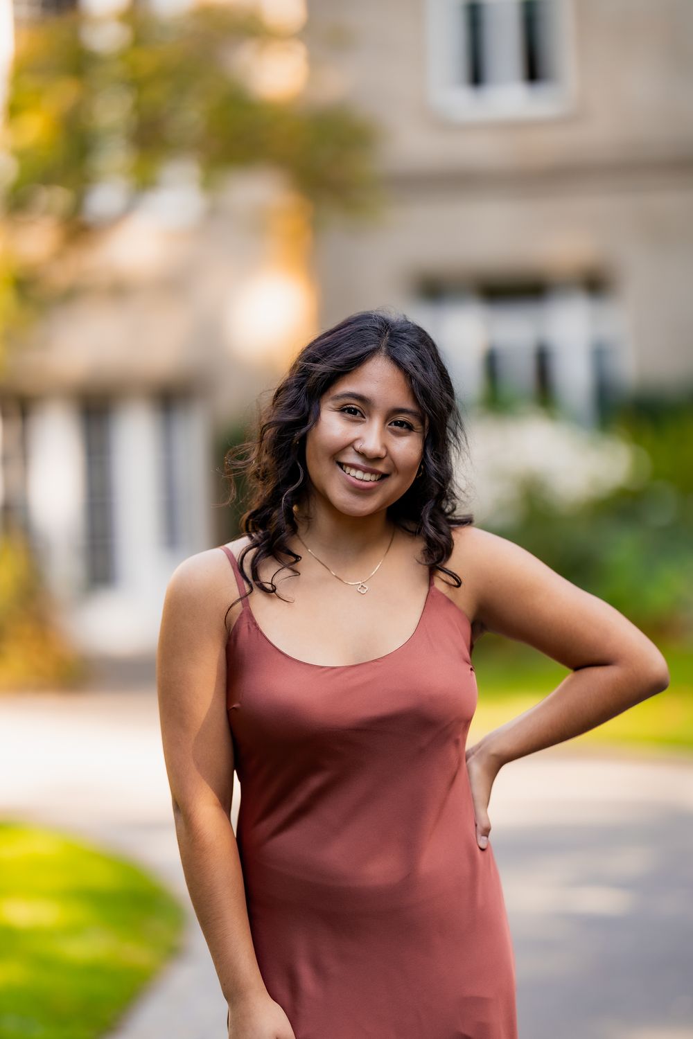 A person in a burgundy tank top poses outdoors with natural bokeh lighting in the background.