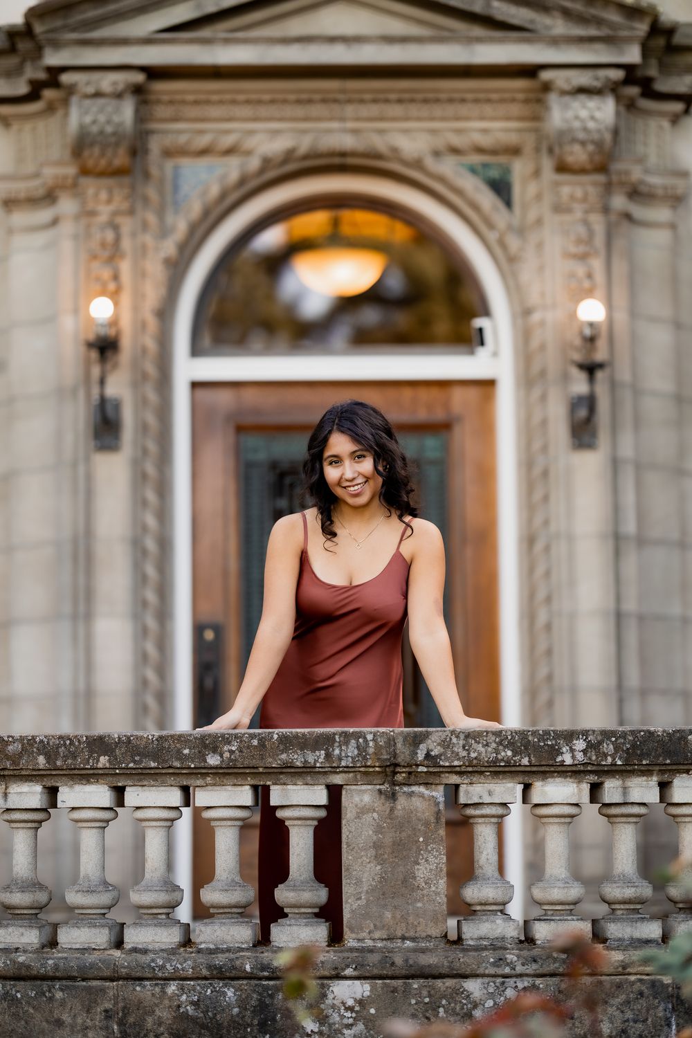 A person in a maroon dress leans against an ornate stone balustrade at a historic building.