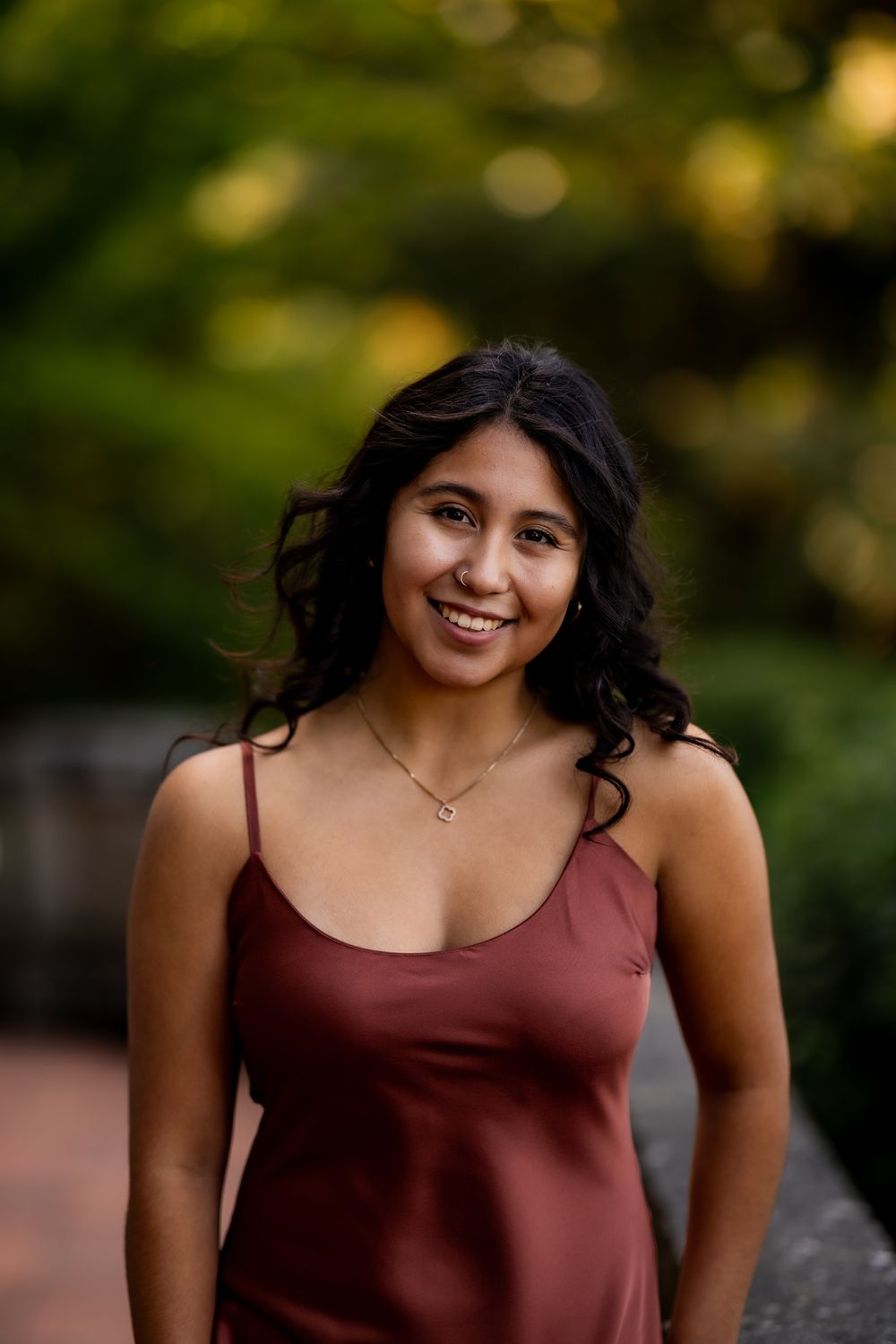 A burgundy dress photographed against a blurred natural background with soft bokeh lighting effects.