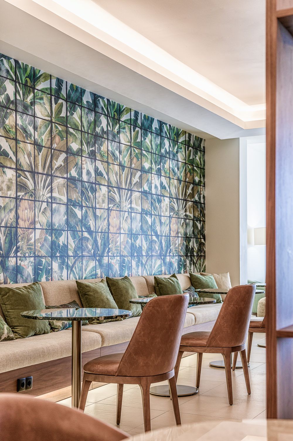 Modern lounge area with tropical leaf wallpaper, brown leather chairs and white bench seating along a curved wall.