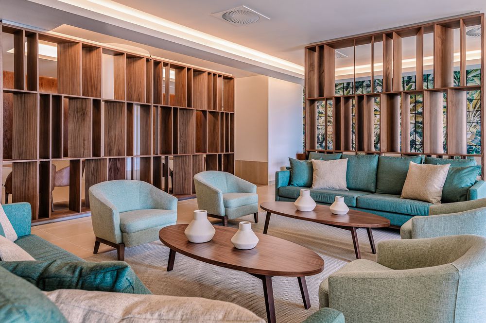 Modern hotel lobby lounge with turquoise and beige seating features wooden divider panels and contemporary lighting design.
