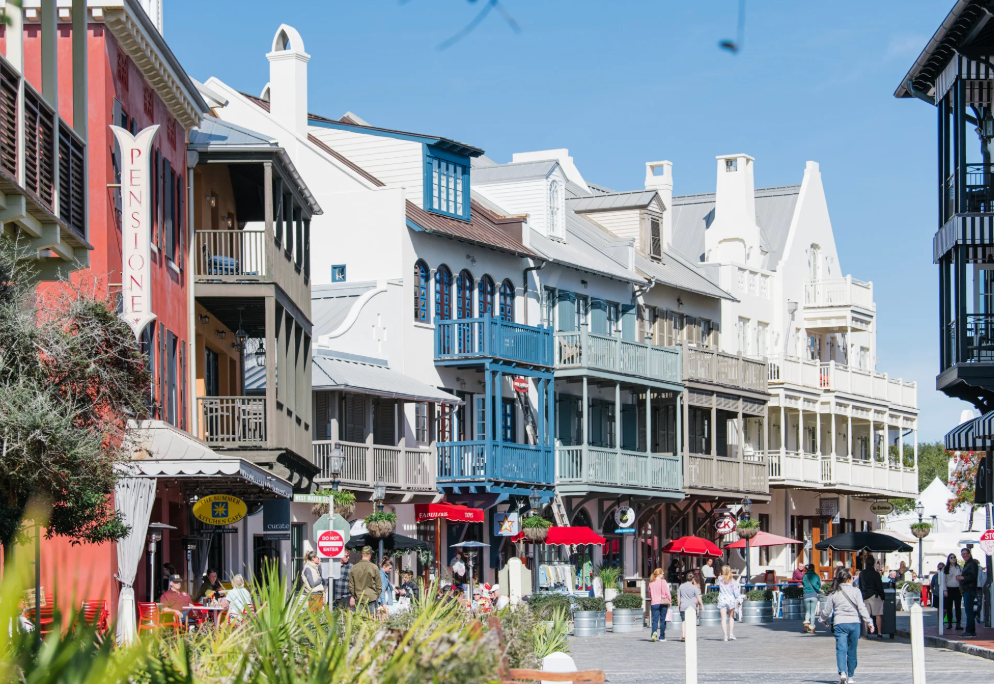 Panoramic view of a charming coastal shopping district with white storefronts and bustling sidewalks on a sunny day.