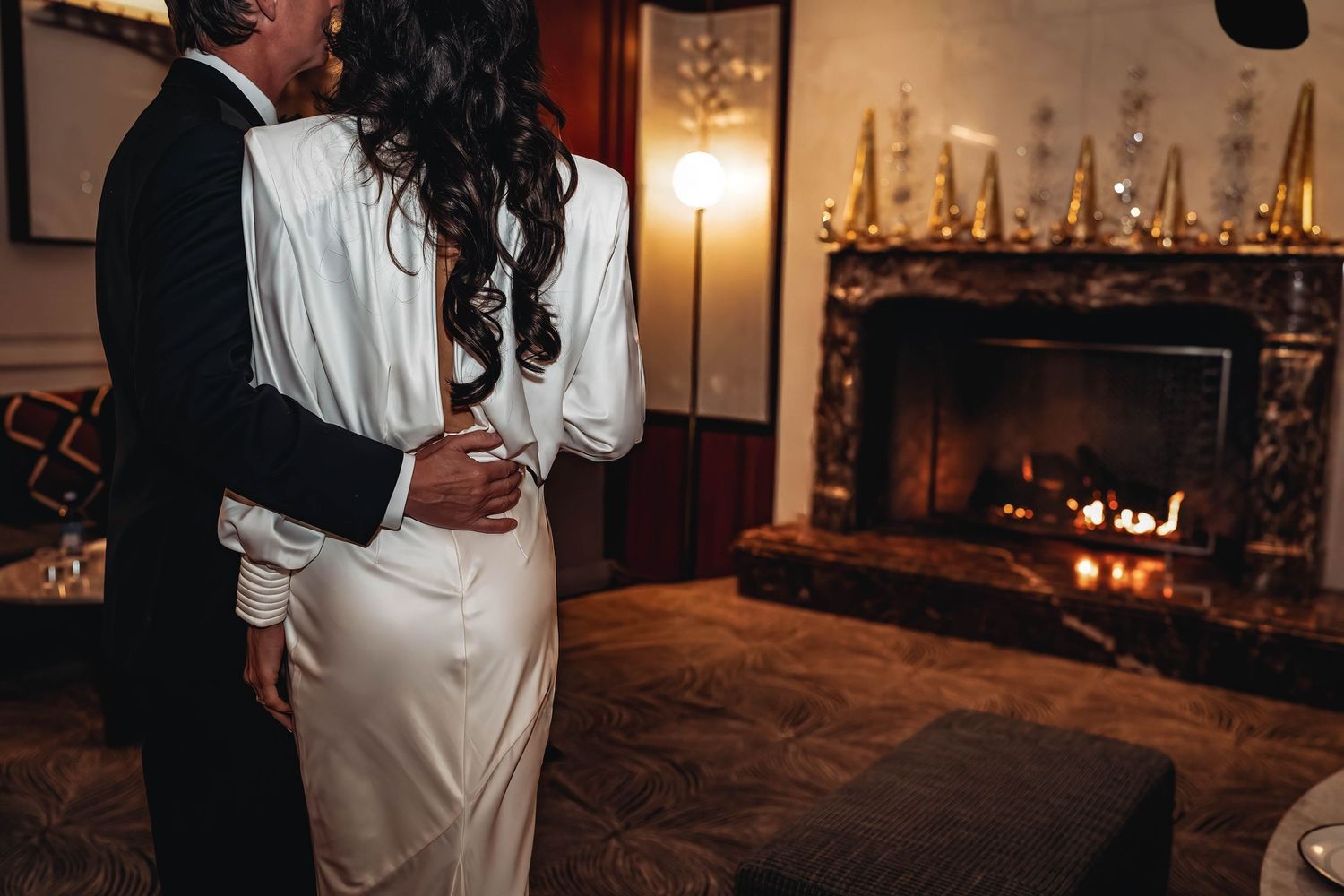 Couple embraces in romantic moment by candlelit fireplace in elegant room with warm ambiance.