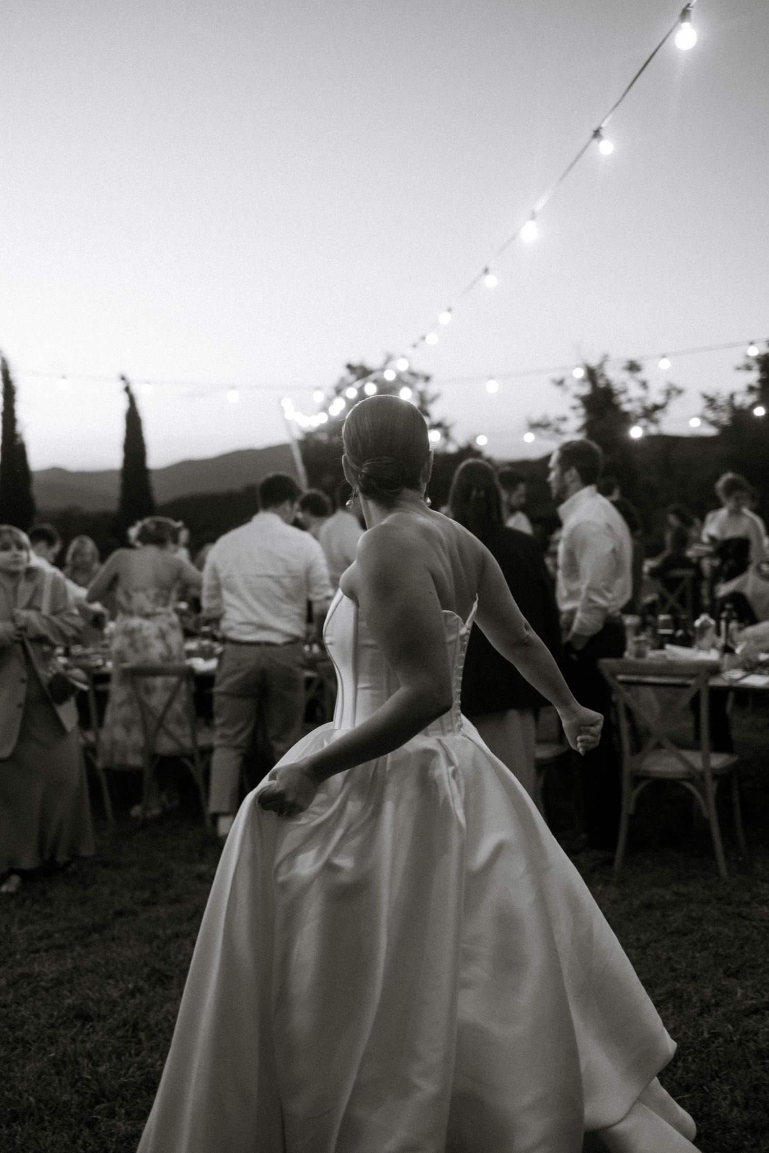 Wedding guests dance and celebrate at an outdoor evening reception with string lights illuminating the festivities.