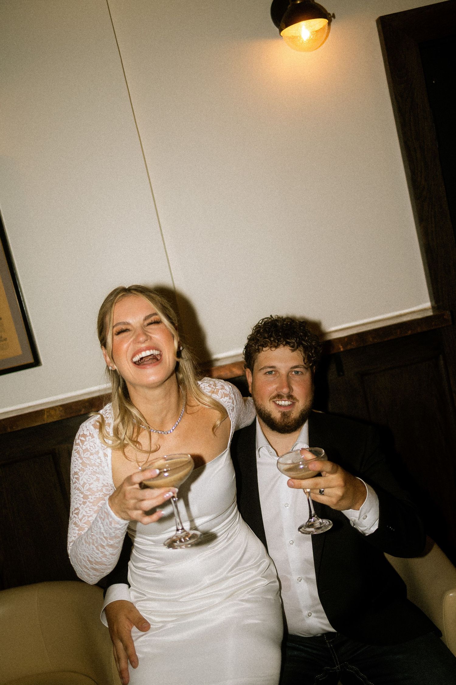 Bride and groom laughing and toasting with martini glasses at their wedding reception.