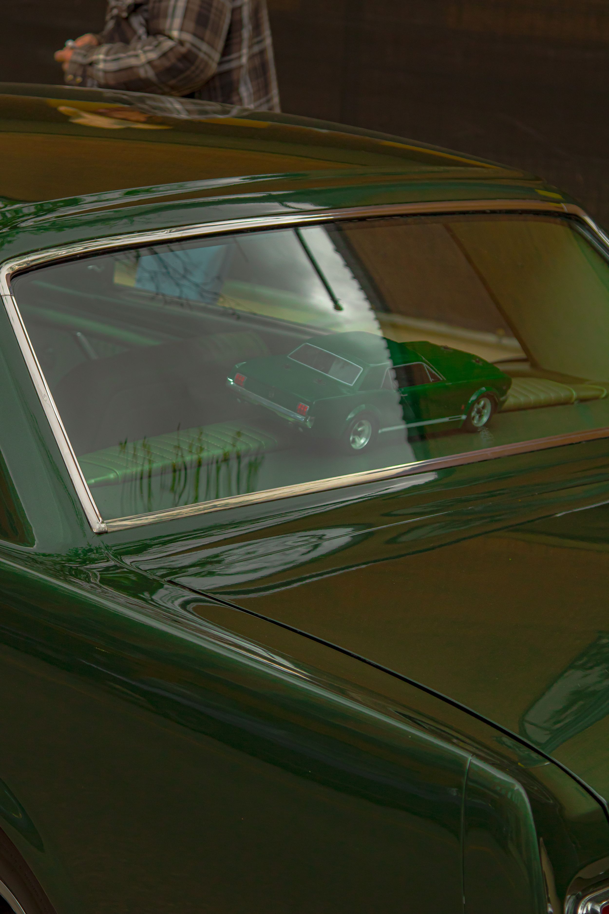 Close-up view of a classic car's glossy green hood and windshield reflecting light in an artistic composition.