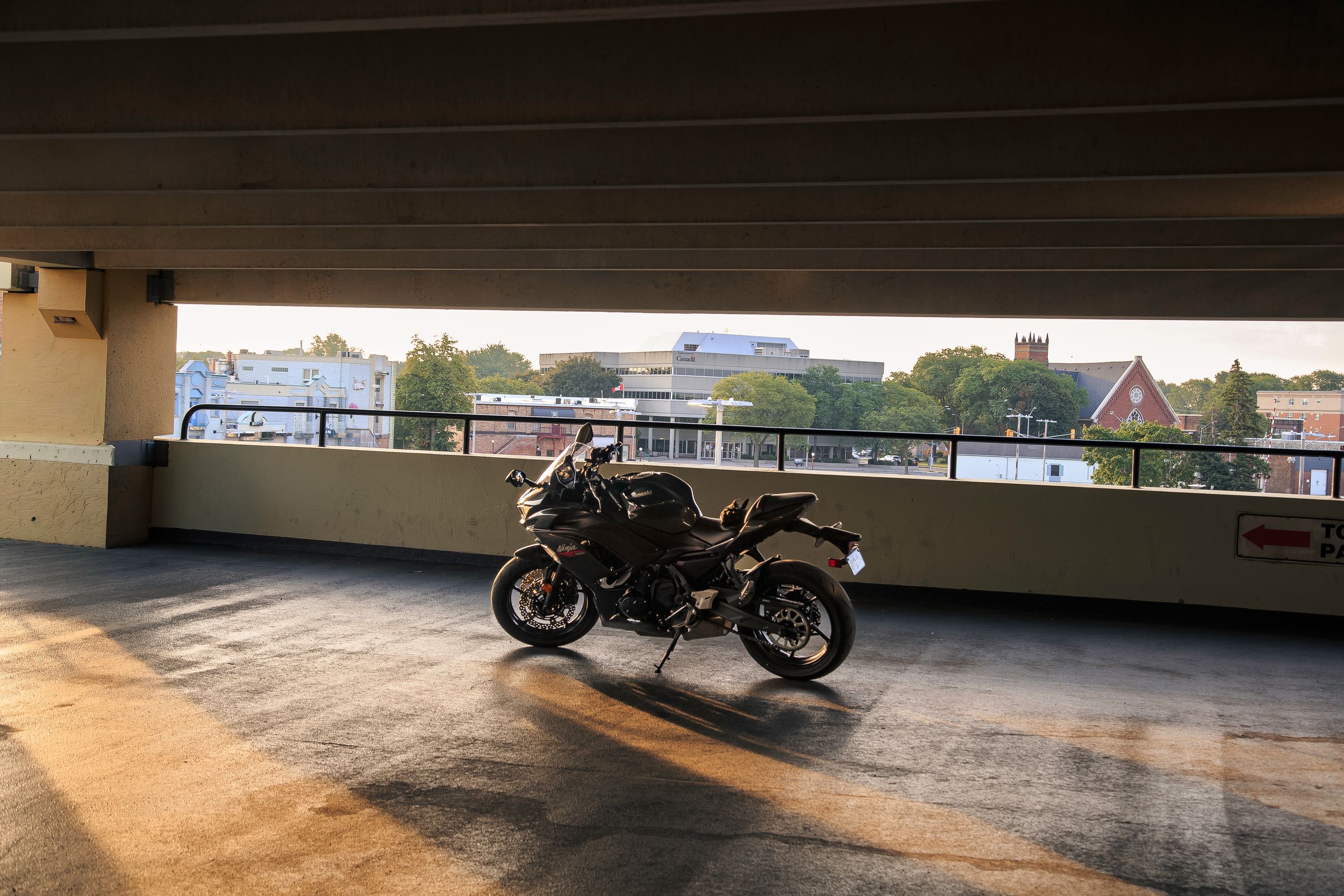 Black sport motorcycle parked on the open top level of a parking garage at sunset with a city skyline and trees in the background.