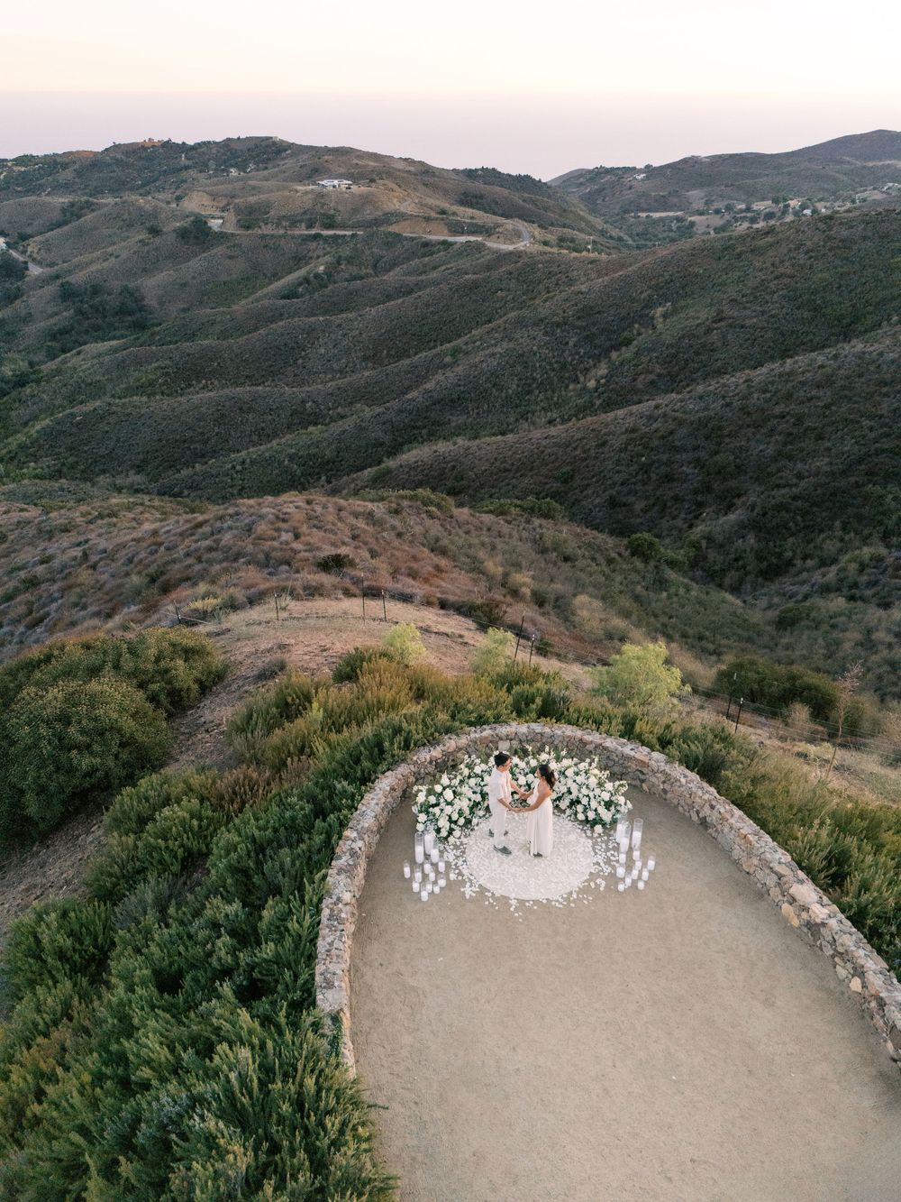 Panoramic view of a hillside outdoor wedding ceremony setup with white chairs arranged in a curved amphitheater style.