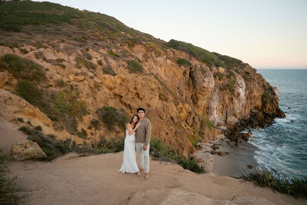Couple poses along rugged coastal cliffs at sunset overlooking the ocean in California.