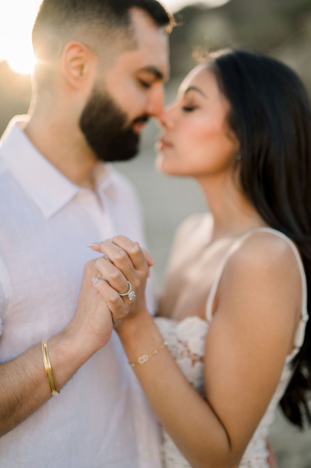 A romantic couple shares an intimate moment while holding hands, showcasing their wedding rings and jewelry.