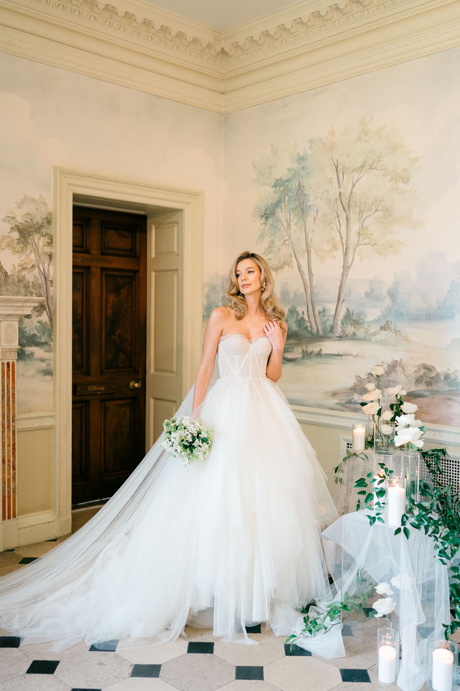 A bride in a flowing white gown twirls gracefully in an elegant room with painted pastoral murals on the walls.