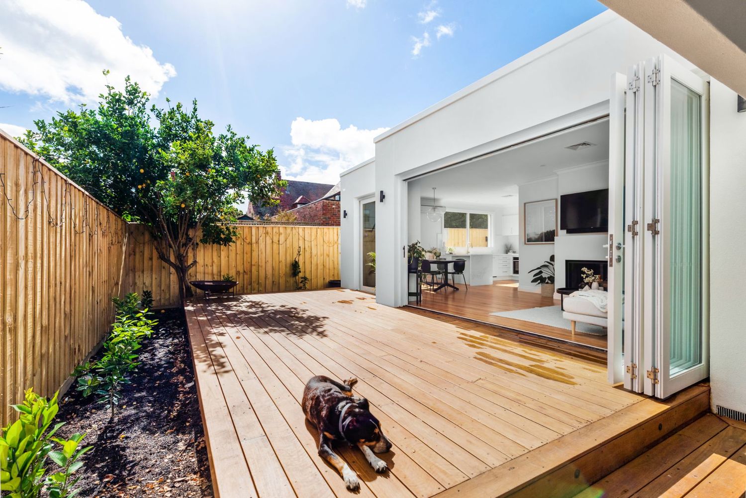 Modern deck space with wooden flooring connecting to interior through folding glass doors.