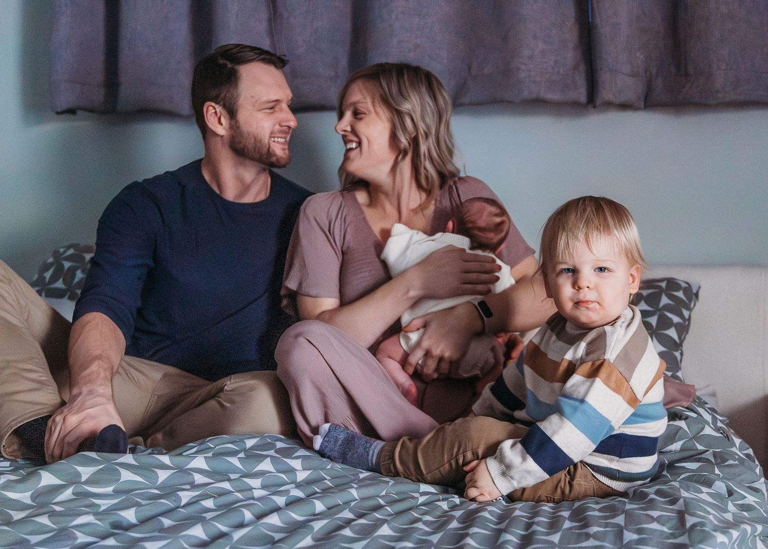 Happy family relaxing together on bed with toddler child in casual home setting.