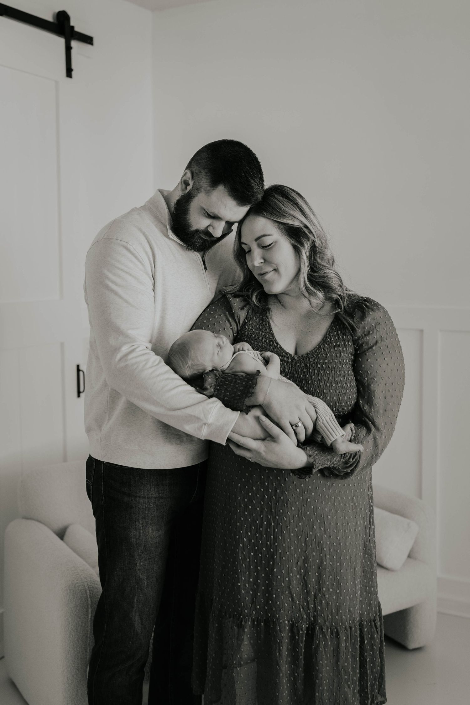 Black and white portrait of parents tenderly cradling their newborn baby in a minimalist white studio newborn session near Minneapolis.
