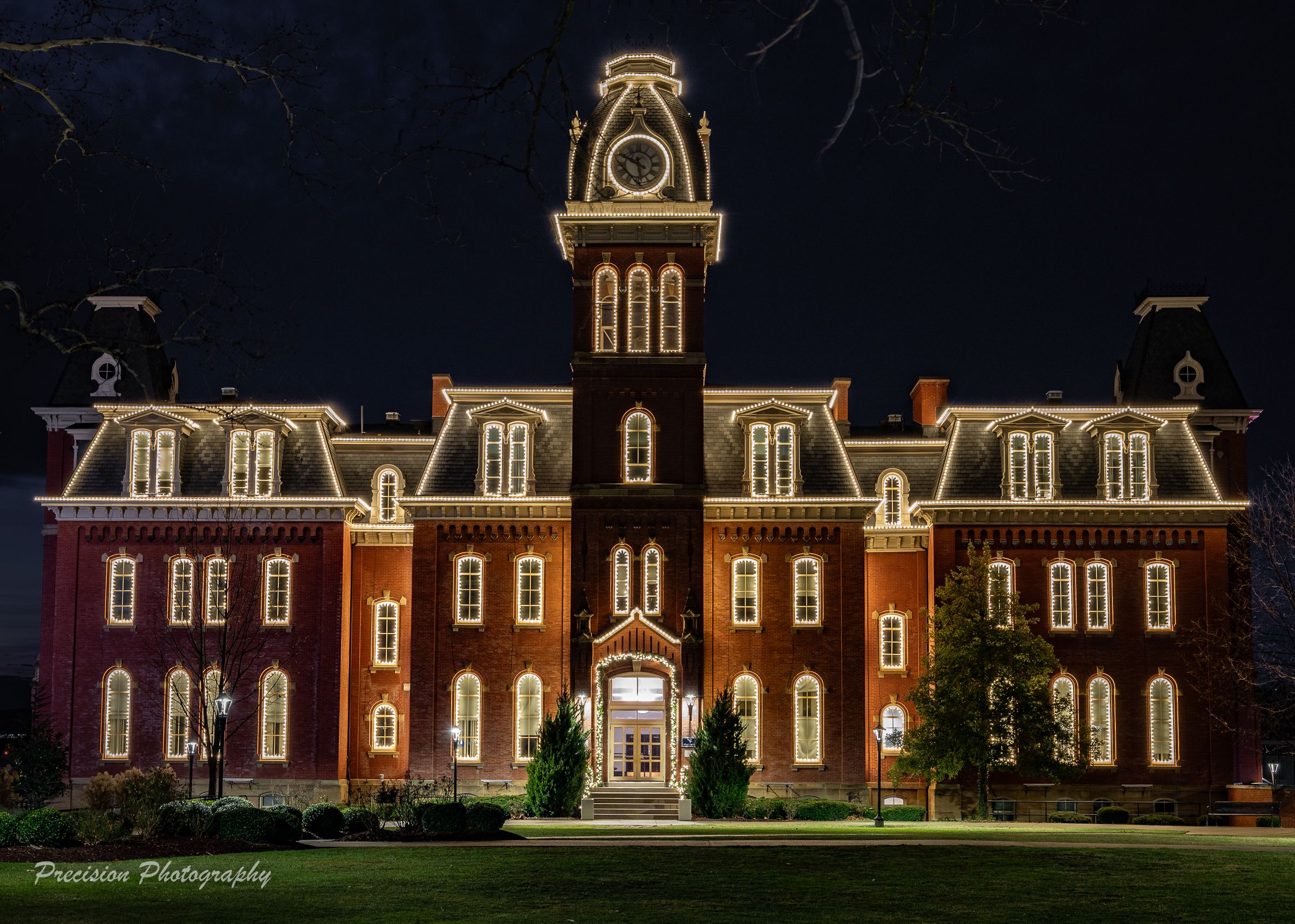 Historic red brick mansion illuminated at night with ornate architectural details and white trim glowing against dark sky.