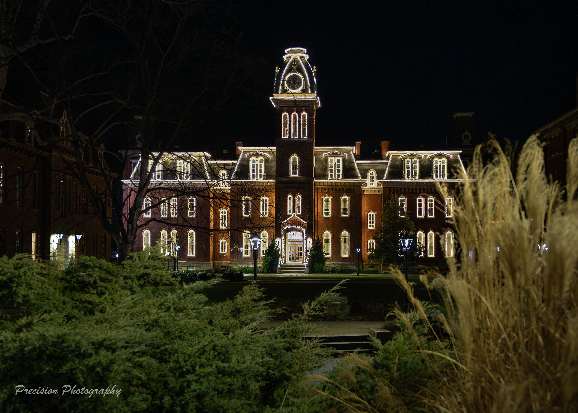 Historic Woodburn Hall at West Virginia University illuminated at night with ornate Victorian architecture and clock tower.