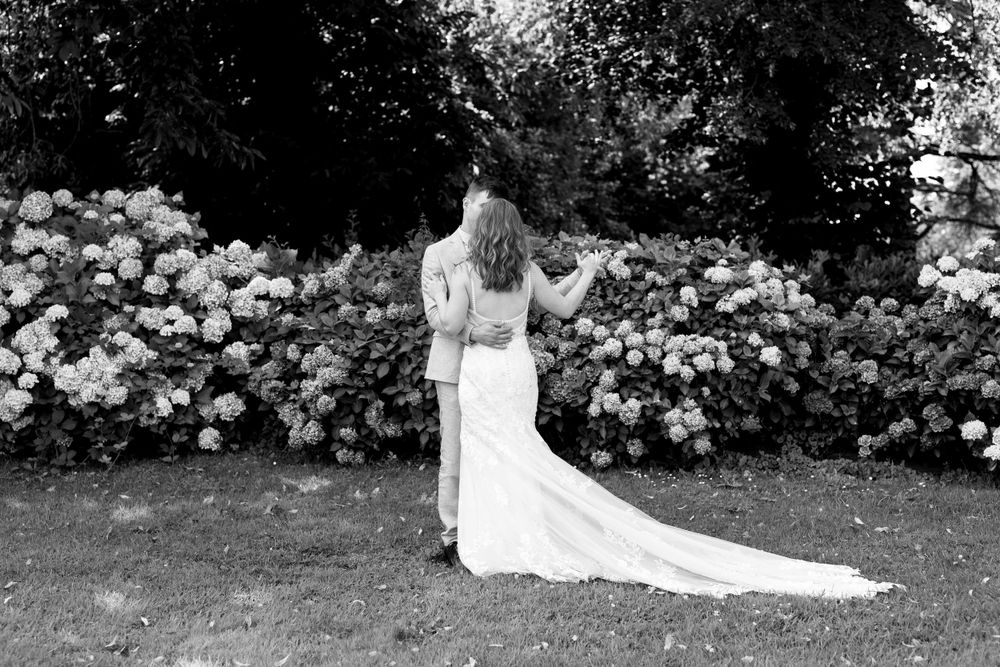 Wedding portraits in a lush garden setting with white flowers blooming in the background.