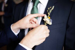 Close-up details of a dark suit jacket with green tie and boutonniere.