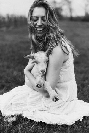 A young goat cuddles on a white blanket in a pastoral outdoor setting.