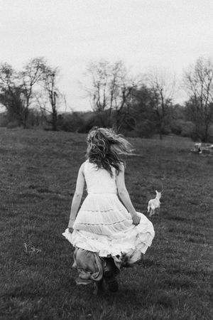 Black and white photo of someone in a flowing white dress running through a pastoral field.