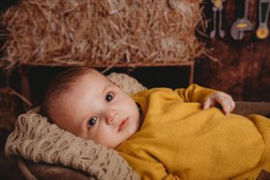 Baby in mustard yellow sweater lying on textured cushion.