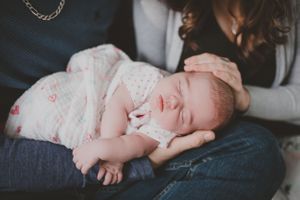 Sleeping newborn wrapped in white patterned blanket resting peacefully on denim-clad lap.