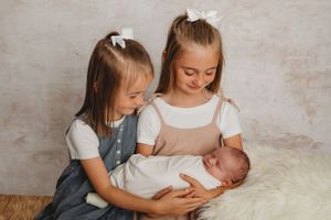 Two children holding and looking down at sleeping newborn on rustic background.